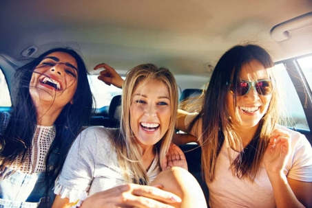 Three women sitting and laughing in the backseat of a vehicle