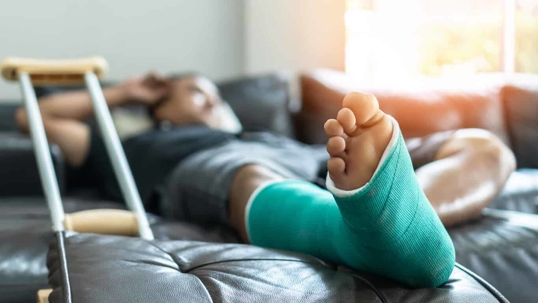 Man lying on sofa with cast on leg, and crutches next to him