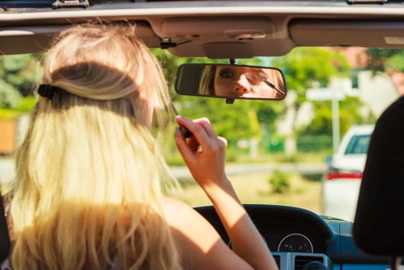 Woman putting on mascara while behind the wheel of her car