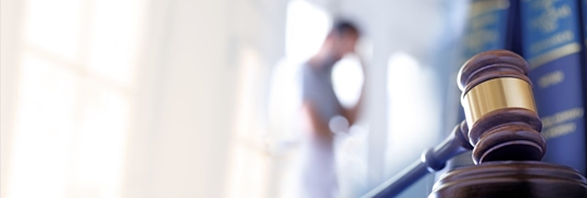 A man stands out of focus in the background behind a gavel and several law books.