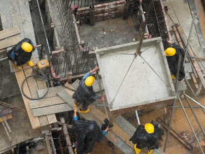 Construction workers in yellow hard hats directing a cement bucket to its location in the pouring rain