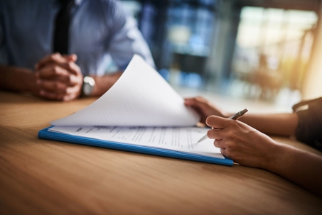 Person holding pen to stack of paper